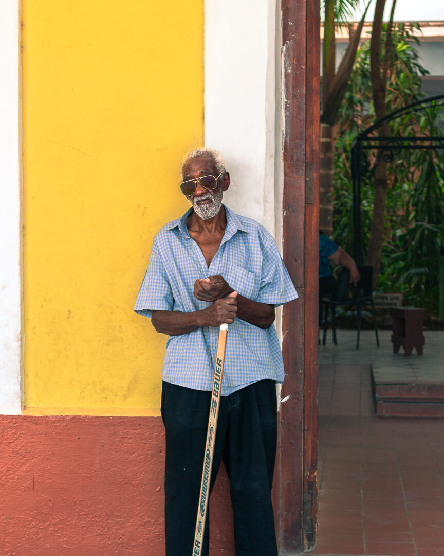 An older man in sunglasses standing against a yellow wall in Trinidad, Cuba